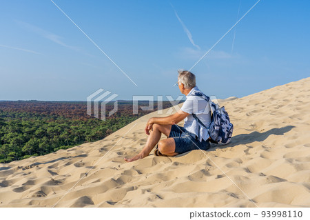 Man sitting on a huge sand dune, famous tourist destination Dune Pyla. Pilat Dune in France.  93998110
