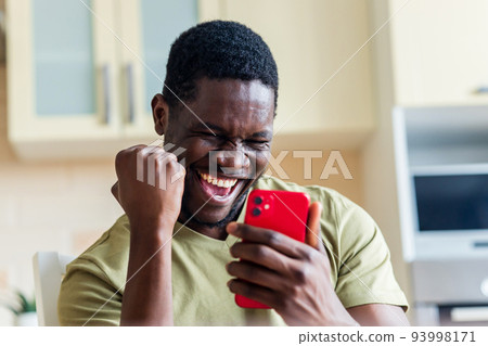 happy afro american man winner excited by mobile app with joy happy afro american man winner excited by mobile app with joy 93998171