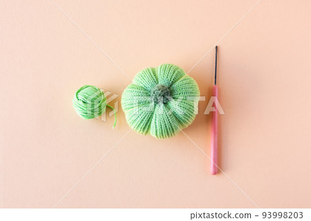 Green knitted pumpkins and an green ball of thread with a crochet hook on a orange background, autumn composition. Halloween concept. Green knitted pumpkins and an green ball of thread with a crochet hook on a orange background, autumn composition. Halloween concept. 93998203