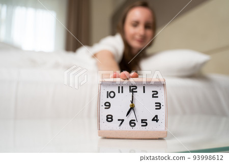Woman wakes up to turn off alarm clock ringing in morning Woman wakes up to turn off alarm clock ringing in morning 93998612
