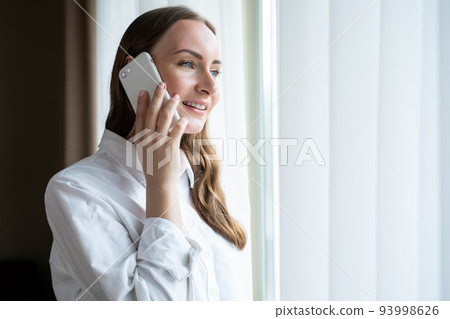 Woman comes to window talking with boyfriend on smartphone Woman comes to window talking with boyfriend on smartphone 93998626