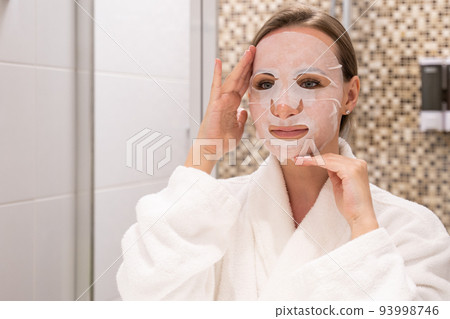 Young woman puts sheet mask on face adjusting with hands 93998746