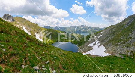 high altitude mountain lake. beautiful nature landscape of romania. grass and snow on the hills. sunny weather with clouds on the sky in summer high altitude mountain lake. beautiful nature landscape of romania. grass and snow on the hills. sunny weather with clouds on the sky in summer 93999069