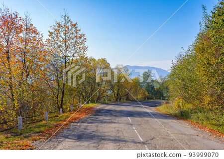 old asphalt rural serpentine in mountains. countryside tourism on a sunny autumn morning. forested hills in colorful foliage. blue sky with fluffy clouds old asphalt rural serpentine in mountains. countryside tourism on a sunny autumn morning. forested hills in colorful foliage. blue sky with fluffy clouds 93999070