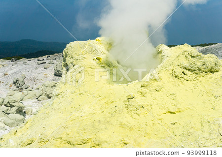 cone of sulfur deposits around a fumarole in a solfataric field illuminated by the sun against a stormy landscape in the distance 93999118