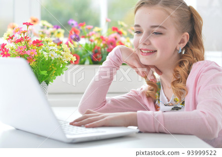Teenage girl sitting at a table with a laptop Teenage girl sitting at a table with a laptop 93999522