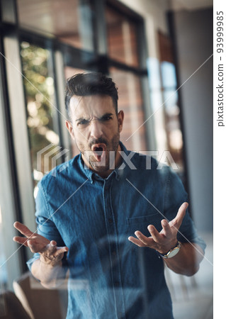 Angry, stressed and frustrated man unhappy and feeling bad about work problems while standing in a modern office alone. Aggressive, annoyed and upset young male filled with emotions screaming loud 93999985
