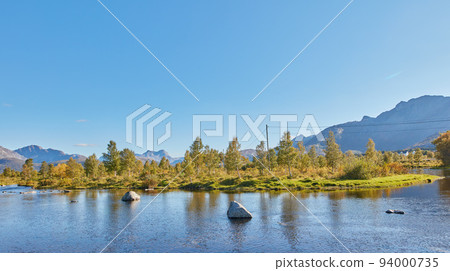 Scenic view of a lake, ocean or sea with blue sky and copy space. Uncultivated trees, bushes, shrubs around a bay of water in Norway. Landscape of calm, serene, peaceful, quiet nature pond with rocks 94000735