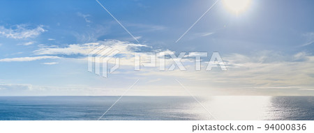 Copy space at sea with the sun in a clear blue sky in the background. Calm ocean tide in an open ocean. A scenic seascape for a relaxing summer holiday with cloudy sky and clean water on the coast 94000836