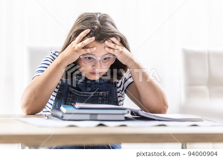 Schoolgirl in glasses tries to comprehend study materials holding her head by both hands Schoolgirl in glasses tries to comprehend study materials holding her head by both hands 94000904