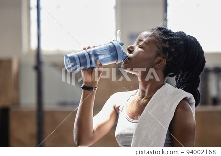 Drinking water and relax after a fitness, workout and exercise training of a woman athlete. Female from Nigeria with sweat done reaching target cardio sports goal at a health, wellness and sports gym Drinking water and relax after a fitness, workout and exercise training of a woman athlete. Female from Nigeria with sweat done reaching target cardio sports goal at a health, wellness and sports gym 94002168