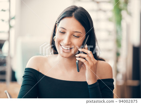 Beautiful young woman talking on a phone call sitting alone at a coffee shop. Confident and friendly female flirting and smiling while calling someone outside a restaurant on a summer weekend 94002875