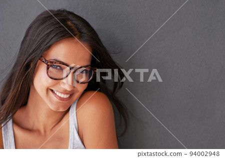 Cool, confident and beautiful woman wearing glasses and smiling with a grey wall and copy space. Face of a cheerful, stunning, attractive and happy female feeling good and showing a positive attitude 94002948