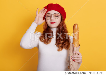Young beautiful woman holding bag of fresh baguette over yellow background, poses with hand on head for mistake, remember error, forgets something important, keeps eyes closed. Young beautiful woman holding bag of fresh baguette over yellow background, poses with hand on head for mistake, remember error, forgets something important, keeps eyes closed. 94003193