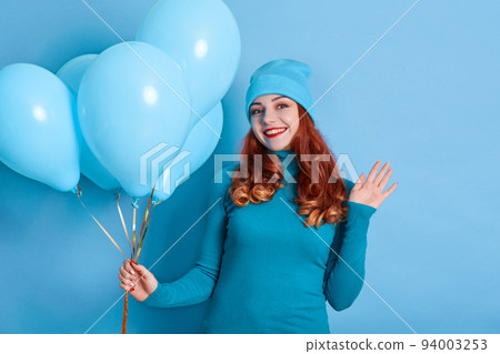 Portrait of attractive female holding in hand bench of balloons, festive celebratory having fun isolated over blue background, smiling girl waving hand to camera. 94003253