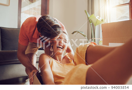 Playful and fun couple moving into their new house, celebrating by being goofy and fooling around. Affectionate boyfriend and girlfriend enjoying their freedom, laughing, bonding and playing 94003854