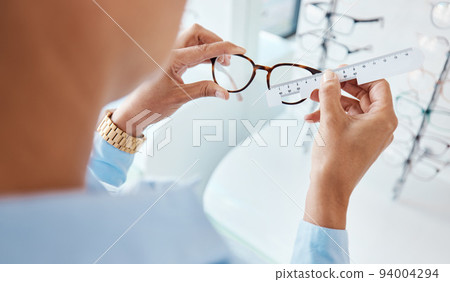Optician or optometrist hands measuring and preparing pair of glasses and frame with optic ruler tool. Eye doctor or ophthalmologist determines visual or vision lens size using special eyewear scale. 94004294
