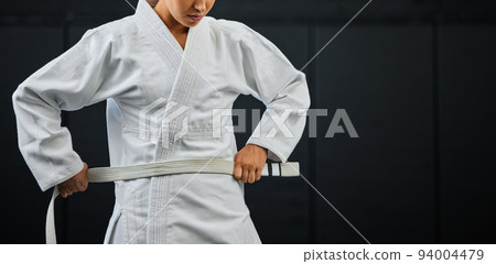 .Beginner, karate and student getting ready for the first day of self defense training against a dark background in a dojo. Determined learner in motivation for fighting lessons in the martial arts. 94004479