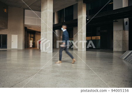 Covid travel regulations for a business man traveling and walking in an airport or hotel. Leaving the office building in hurry, being late or rushing after working overtime in a city or urban town Covid travel regulations for a business man traveling and walking in an airport or hotel. Leaving the office building in hurry, being late or rushing after working overtime in a city or urban town 94005156