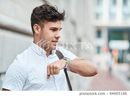 Chatting on a smartwatch with a young creative business man or intern commuting in the city. Hailing a cab, taxi or ride with an app on wireless technology. Male employee travelling to and from work 94005186