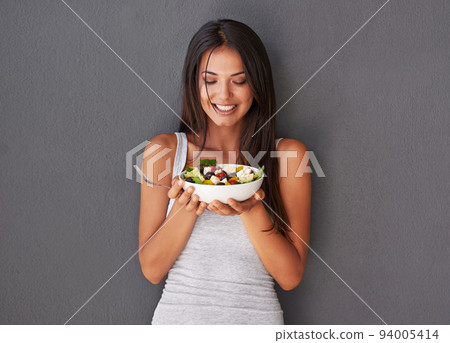 Healthy young female eating her fresh food salad bowl. Smiling beautiful woman holding and enjoying eating her clean green diet dish of vegetables as part of her vegan wellness lifestyle Healthy young female eating her fresh food salad bowl. Smiling beautiful woman holding and enjoying eating her clean green diet dish of vegetables as part of her vegan wellness lifestyle 94005414