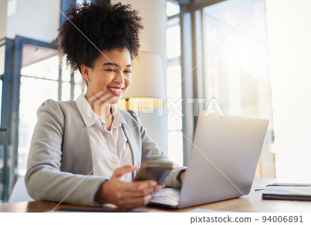 Happy corporate employee texting on a phone while working on a laptop in an office, reading email. Young professional assistant multitasking to complete an online task, efficient time management Happy corporate employee texting on a phone while working on a laptop in an office, reading email. Young professional assistant multitasking to complete an online task, efficient time management 94006891