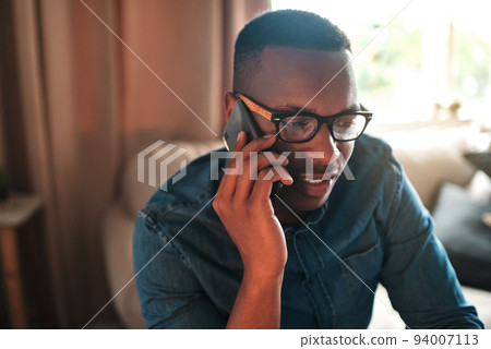 Young student talking on a phone call to a friend, colleague or family member. Black male university or college learner studying design, marketing or architecture sitting and chatting at home 94007113