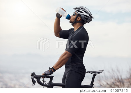 Sports man with a bike drinking water bottle doing fitness training or workout on sky mockup background. Healthy, professional athlete cyclist with a bicycle during cycling cardio exercise in nature 94007245