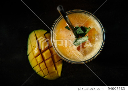 An invigorating non-alcoholic cocktail with mango pulp, mint leaves and ice cubes. Flat lay. An invigorating non-alcoholic cocktail with mango pulp, mint leaves and ice cubes. Flat lay. 94007383