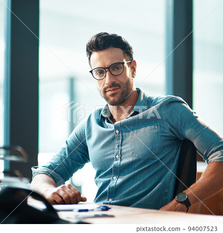 Young, confident and professional business man wearing glasses, sitting at his desk and working in a modern office portrait. A casual and serious corporate male in the finance department Young, confident and professional business man wearing glasses, sitting at his desk and working in a modern office portrait. A casual and serious corporate male in the finance department 94007523
