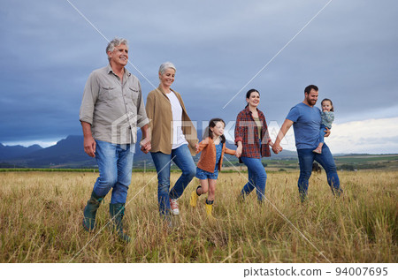 Big happy family walking on field, meadow and countryside in nature to relax, bond and holding hands in love, trust and support. Generation of grandparents, parents and kids having fun outside 94007695