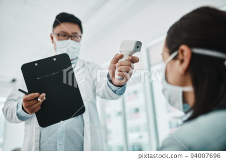 Doctor scanning the temperature of a patient for corona with a digital thermometer. Health care professional consulting with a concerned female about flu symptoms during the covid virus pandemic Doctor scanning the temperature of a patient for corona with a digital thermometer. Health care professional consulting with a concerned female about flu symptoms during the covid virus pandemic 94007696