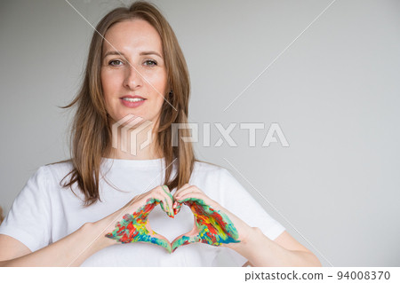 Brown-haired woman shows heart with painted hands in studio Brown-haired woman shows heart with painted hands in studio 94008370