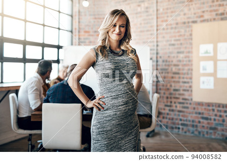 Modern and professional pregnant businesswoman smiling and standing in a leadership role, in a meeting with work colleagues. Ambitious mother working in management of casual business startup Modern and professional pregnant businesswoman smiling and standing in a leadership role, in a meeting with work colleagues. Ambitious mother working in management of casual business startup 94008582