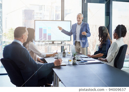 Sales manager gives a presentation on marketing and brand strategy in a boardroom meeting. Successful, corporate and mature male leader points to a graph on the monitor screen to show the planning 94009637