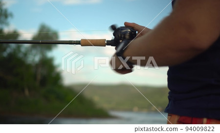 A professional fisherman catches a fish by spinning. Hands and fishing rod close-up. A man stands in a boat and sways on the waves. A professional fisherman catches a fish by spinning. Hands and fishing rod close-up. A man stands in a boat and sways on the waves. 94009822
