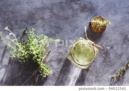 Thyme essential oil in open bottle, cork and fresh Thymus plants on gray marble table, flat lay 94012542