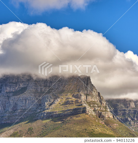 Clouds covering top of Table Mountain, Cape Town with copyspace. Cloud shape and shadow over rocky terrain on a sunny day, beautiful, calm nature in harmony with scenic views of plants and landscape 94013226