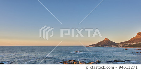 Ocean view of sea water on rocky beach, mountains and a blue sky with copy space of Lions Head in Cape Town, South Africa. Calm tide, serene and tranquil scenery of relaxing mother nature at sunrise 94013271