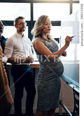Pregnant businesswoman doing a presentation in a meeting planning the company growth strategy in an office. Serious female entrepreneur briefing her team on the startup project mission and vision 94013309