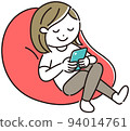 A woman relaxing while looking at her smartphone on a bead cushion 94014761