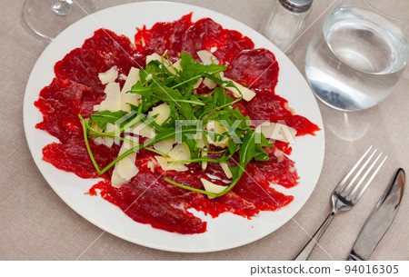 Thin slices of meat carpaccio, cheese and arugula on white plate. Traditional Italian dish 94016305