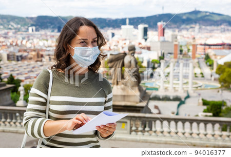 Girl traveler in protective mask with a guidebook in her hands on the street of european city Girl traveler in protective mask with a guidebook in her hands on the street of european city 94016377