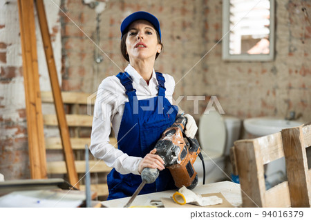 Female builder confidently holding pneumatic jackhammer in house under construction Female builder confidently holding pneumatic jackhammer in house under construction 94016379