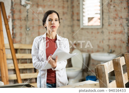 Female designer with papers working in apartment under renovation Female designer with papers working in apartment under renovation 94016433