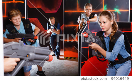 Happy teen brother and sister standing with laser pistols during laser tag game with parents in labyrinth Happy teen brother and sister standing with laser pistols during laser tag game with parents in labyrinth 94016449