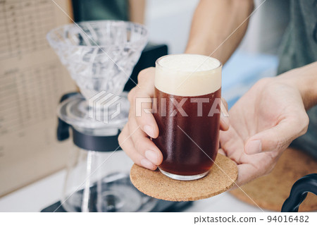 Barista holding and serving a drinking glass of cold brew dip coffee. Barista holding and serving a drinking glass of cold brew dip coffee. 94016482