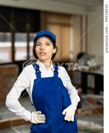 Woman foreman in blue overalls posing in house under construction 94016650