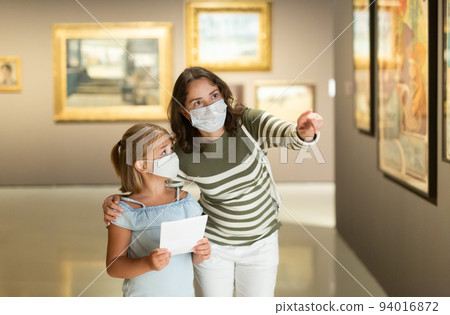 Mom and daughter in protective masks inspect the exhibits of museum 94016872