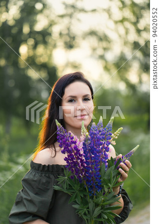An attractive woman in a field with a summer bouquet of wildflowers Lupinus. Vertical photo. 94020552